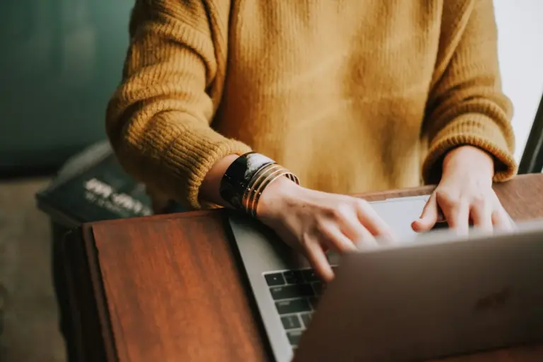 Person im gelben Pullover tippt auf einem Laptop