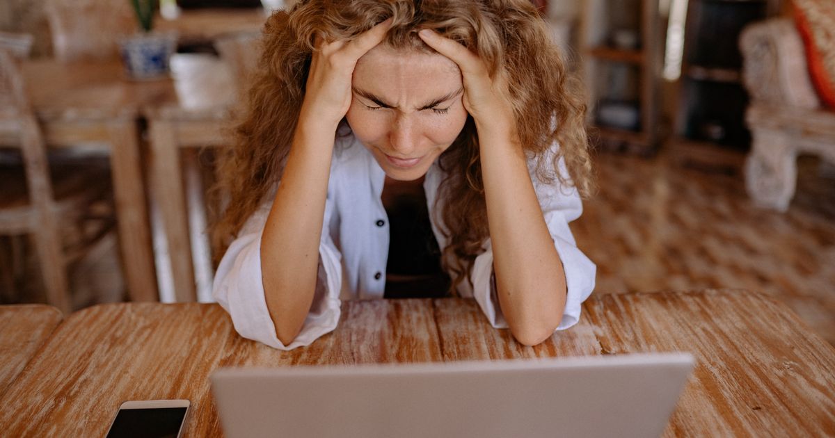 Frau sitzt besorgt am Laptop mit dem Handy daneben, weil sie ihr Gmail Passwort vergessen hat